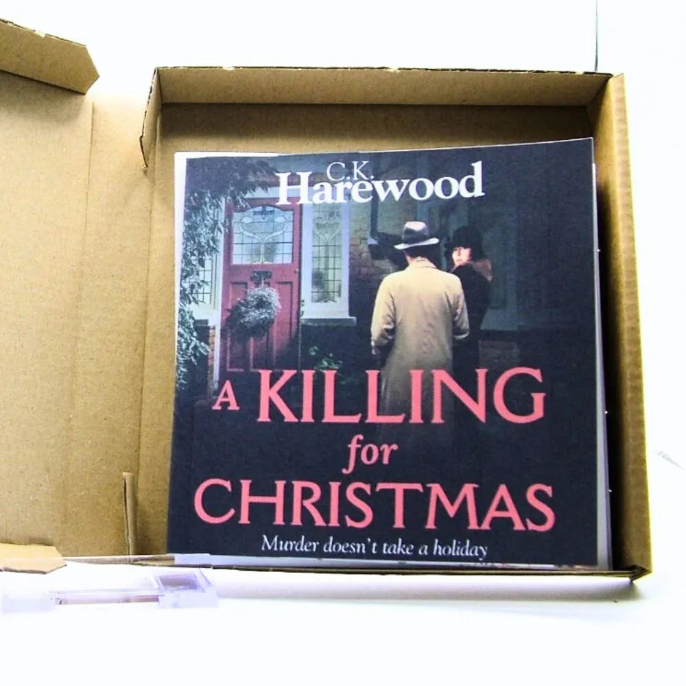 Book titled 'A Killing for Christmas' by C.K. Harewood inside a cardboard box.