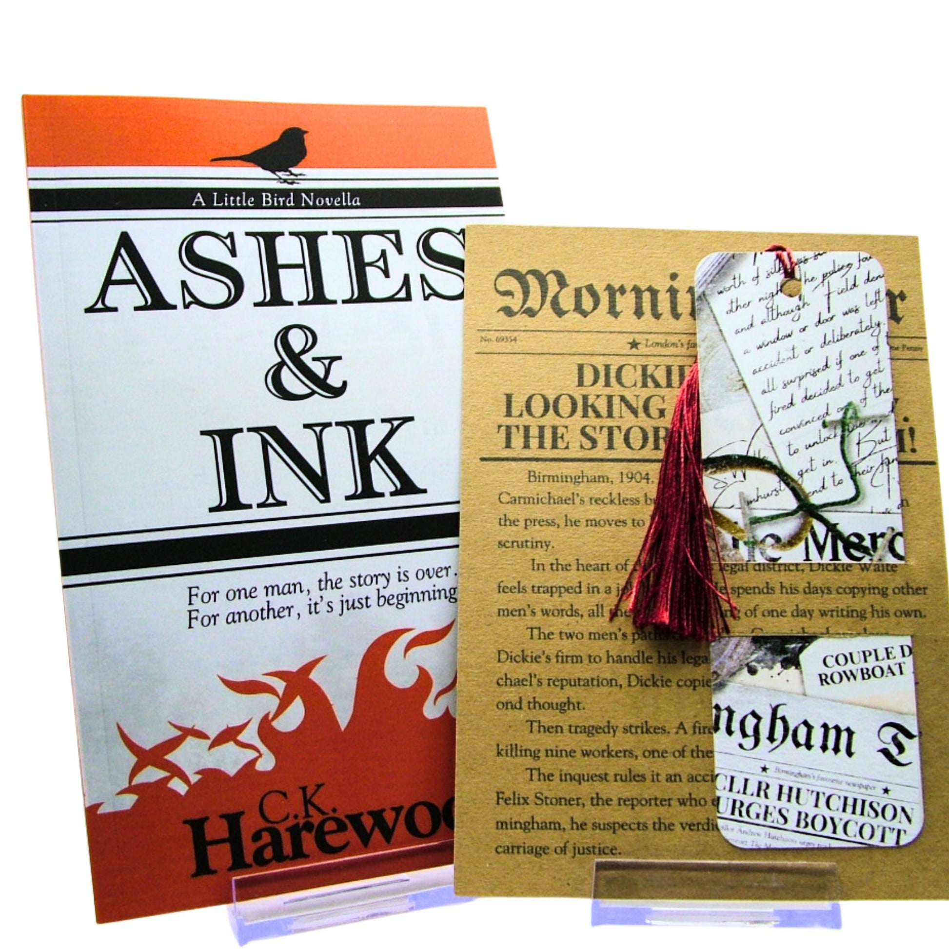 Book titled 'Ashes & Ink' by C.K. Harewood with a tasselled bookmark and paper item on a white background