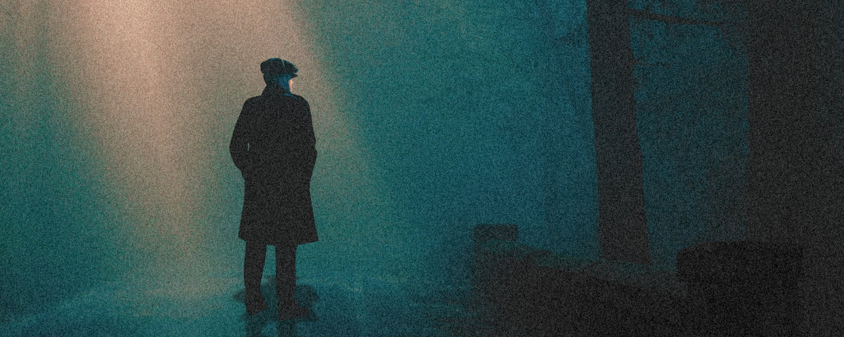 A dark silhouette of a person standing in a misty, blue-toned outdoor scene with a spotlight shining down from the upper left.